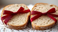 Fresh baked bread slices tied with red ribbon bows on white lace doily, rustic bakery gift concept for holidays and special occasions.