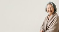 Senior woman with gray hair wearing beige cardigan, smiling warmly at camera against neutral background. Suitable for healthcare, wellness, lifestyle and aging-related content.