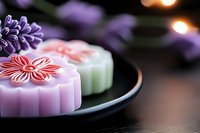 Traditional Asian mooncakes with delicate floral decorations in pink and purple on black plate with soft bokeh background, close-up view showing intricate details.