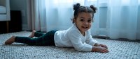 Adorable African American toddler girl crawling on carpet in bright living room with natural window light, exploring and learning developmental milestone.