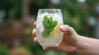 Refreshing lemonade with fresh mint leaves and ice cubes held in hand outdoors, perfect for summer beverages, cocktails, and drink photography.