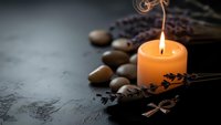 Glowing orange candle with spa stones and dried lavender creating peaceful wellness atmosphere on dark textured surface for relaxation and meditation.