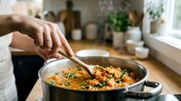 Person stirring healthy vegetable stew in pot with wooden spoon in modern kitchen. Home cooking, nutritious meal preparation, comfort food concept.