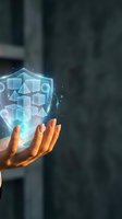 Hand holding glowing digital shield with geometric shapes representing cybersecurity protection and data security technology in modern business environment.