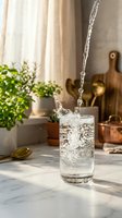Fresh sparkling water pouring into glass on marble counter in modern kitchen with natural sunlight and green plants creating healthy lifestyle scene.