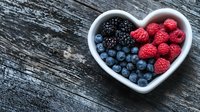 Fresh mixed berries in heart shaped white bowl on rustic wooden background. Healthy organic raspberries, blueberries and blackberries for natural food concept.