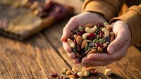 Hands holding mixed nuts and dried fruits on rustic wooden table. Healthy snacking, organic food ingredients for cooking and baking recipes.