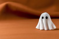 Cute white ghost figure with black eyes on orange background, minimal Halloween decoration concept for seasonal designs and festive projects.