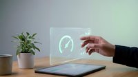 Young adult hand interacting with glowing speedometer hologram on desk workspace with tablet and potted plant for technology, digital innovation, and business solutions concepts.