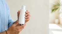 Man with dark skin tone holding white cosmetic bottle for skincare, lotion, or personal care product advertising and promotional use.