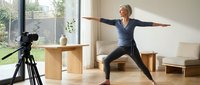 Senior woman in warrior pose during online yoga class, demonstrating flexibility and strength for fitness instruction and wellness content.
