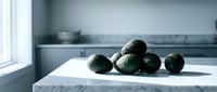 Fresh ripe avocados arranged on marble kitchen counter near window with natural lighting and modern kitchen background for healthy cooking concepts.