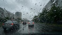 Heavy rain drops on car windshield with blurred traffic and red brake lights creating atmospheric driving conditions during stormy weather.