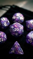 Purple glitter polyhedral dice set with white numbers on black velvet surface, perfect for tabletop gaming, role-playing games, and dungeon master collections.