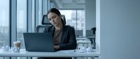 Professional businesswoman working on laptop in modern office environment with city view windows for corporate presentations and workplace concepts.