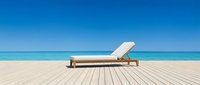 Wooden lounge chair with white cushion on beach deck overlooking turquoise ocean and clear sky, perfect for travel and vacation marketing.