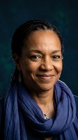 Mature African American woman with braided hair smiling warmly in blue scarf against dark background for professional headshot and portrait photography.