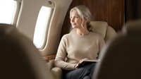 Senior Caucasian woman relaxing in luxury private jet cabin during flight. Business travel comfort and premium aviation services for mature passengers.