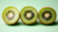 Fresh kiwi fruit halves arranged in row showing detailed cross sections with distinctive star pattern and black seeds against mint green background.