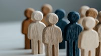 Wooden figures standing in line showing diversity and inclusion concept, with one dark blue figure among light colored ones, representing uniqueness and leadership.
