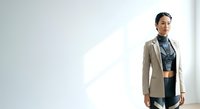 Professional woman with South Asian ethnicity wearing casual blazer and crop top standing in minimalist white interior space with natural light for lifestyle and fashion content.