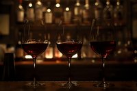 Three glasses of red wine on wooden bar counter with blurred bottles in background. Elegant setting for wine tasting or upscale restaurant atmosphere.
