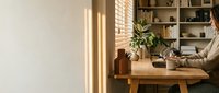 Cozy home office workspace with wooden desk, laptop, plants and natural lighting creating productive work from home environment for remote professionals.