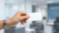 Hand holding blank white business card in modern office environment with blurred background, suitable for corporate branding and professional identity design projects.