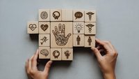 Hands arranging wooden blocks with healthcare and medical symbols including brain, heart, caduceus for wellness concept design.