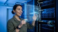 Female IT professional with dark hair and olive complexion interacting with holographic data visualization in server room, managing network infrastructure and cloud computing systems.