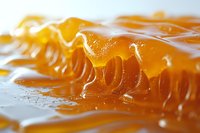 Fresh honeycomb with golden honey dripping and flowing in macro close up view, showing natural organic texture and sweet amber liquid patterns.