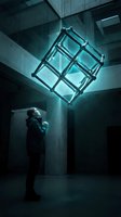 Man in dark jacket standing in concrete industrial space gazing up at glowing neon cube structure suspended above, symbolizing innovation, technology, and future vision for business concepts.