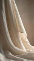 Soft beige linen fabric draping elegantly with natural folds and warm lighting creating cozy textile atmosphere for home decor and fashion design projects.