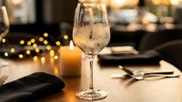 Elegant wine glass filled with sparkling champagne on restaurant table with warm candlelight and bokeh lights creating romantic dining atmosphere for celebrations.
