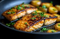 Grilled salmon fillets with golden crust and fresh herbs served with roasted potatoes in cast iron pan, close up view showing juicy texture and caramelized surface.