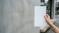 Hand holding blank white paper sheet against urban concrete wall background for mockup and branding purposes.