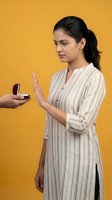 Young South Asian woman refusing marriage proposal ring box with hand gesture on yellow background for relationship and decision concepts.