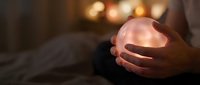 Hands gently holding glowing orb of warm light in dark cozy bedroom setting. Concept of hope, healing energy, meditation and spiritual wellness practices.