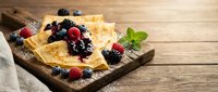 Fresh crepes with mixed berries and mint on rustic wooden board. Delicious breakfast or dessert presentation with blackberries, raspberries on wood table.