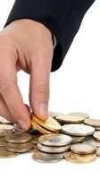 Caucasian male hand in business suit picking gold coins from a pile of mixed currency, symbolizing wealth, savings, and financial success.