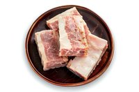 Fresh raw pork ribs with meat and fat layers on brown ceramic plate isolated on white background, ready for cooking or grilling preparation.