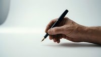 Male hand holding black pen ready to write on white paper surface for business documents contracts signatures and office work.