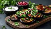 Grilled eggplant slices topped with fresh herbs, pomegranate seeds and yogurt sauce on wooden serving board against dark background, appetizer presentation.