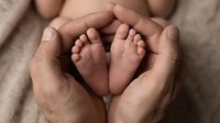 Adult hands cradling newborn baby feet in heart shape on neutral fabric background. Parenthood, family bonding, and new life concept for healthcare and maternity designs.