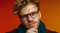 Young man with curly hair and glasses wearing teal scarf against vibrant orange-red gradient background, thoughtful expression with hand on chin.