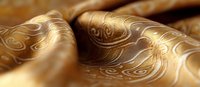 Luxurious golden silk fabric with elegant swirling pattern creates soft waves and folds, showcasing intricate oriental motifs in close-up macro photography.