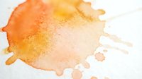 Abstract watercolor splash in warm orange and yellow tones with organic flowing edges on white background for creative design projects.
