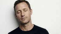 Middle-aged Caucasian man with closed eyes and peaceful expression wearing black shirt against neutral background for wellness and mindfulness concepts.