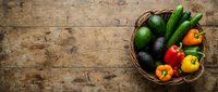 Fresh organic vegetables in wicker basket on rustic wooden table. Avocados, cucumbers, peppers and tomatoes for healthy cooking and meal preparation.
