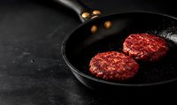 Raw beef patties cooking in black cast iron pan on dark background. Fresh ground meat burgers grilling with oil drops, minimalist food photography for restaurant menu.